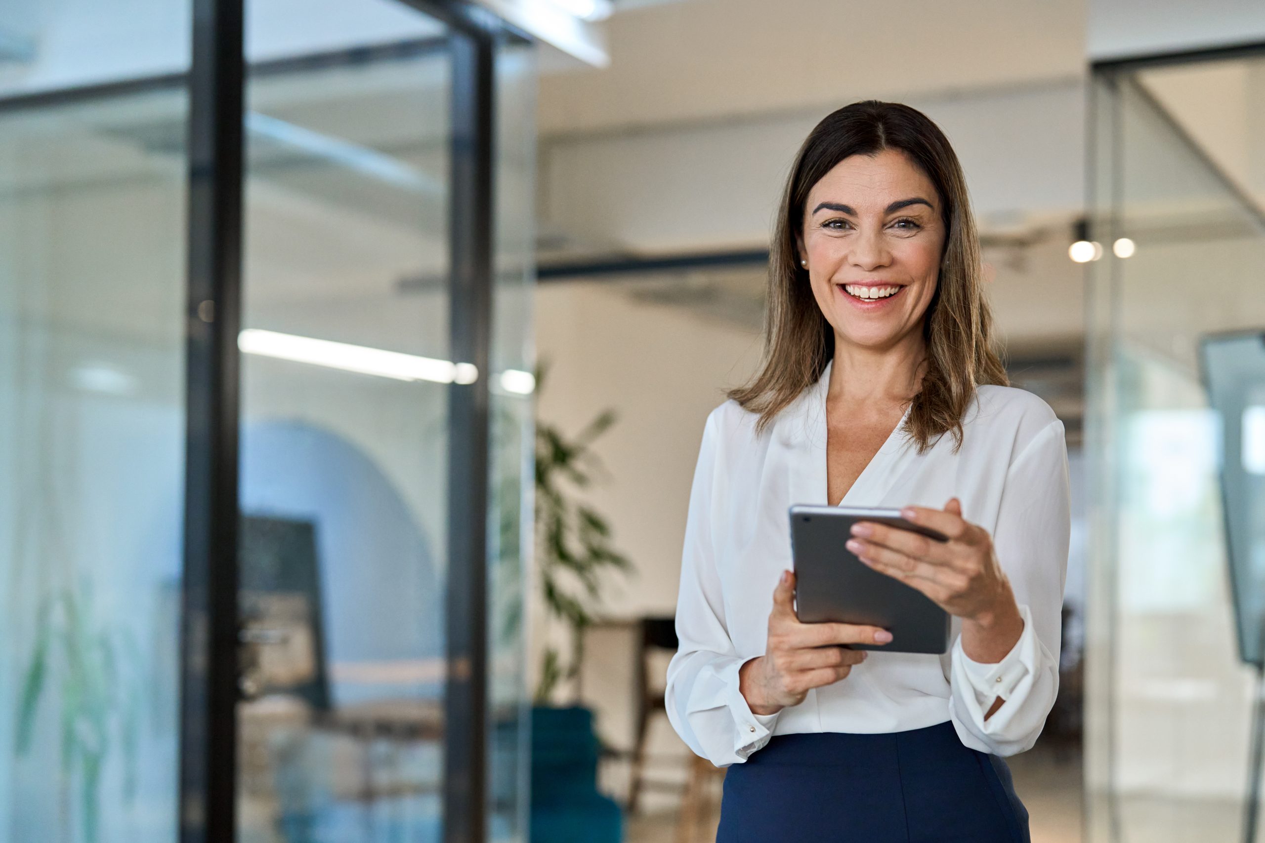 Smiling mature business woman executive holding tablet in office. Portrait.