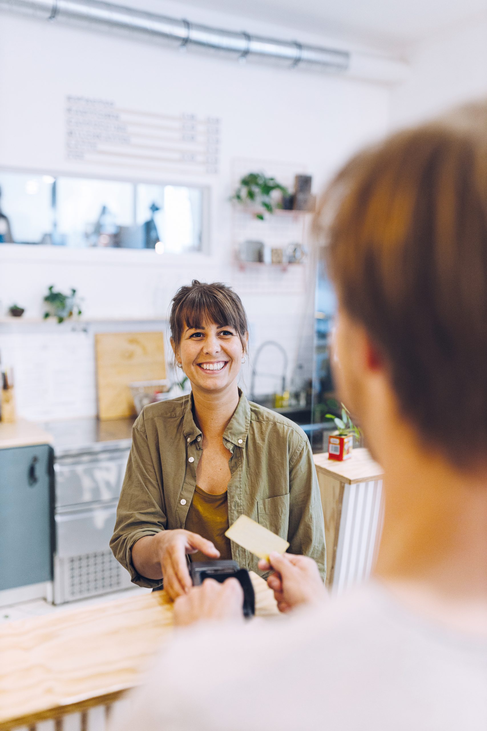 Male customer paying with credit card to female owner at checkout in coffee shop