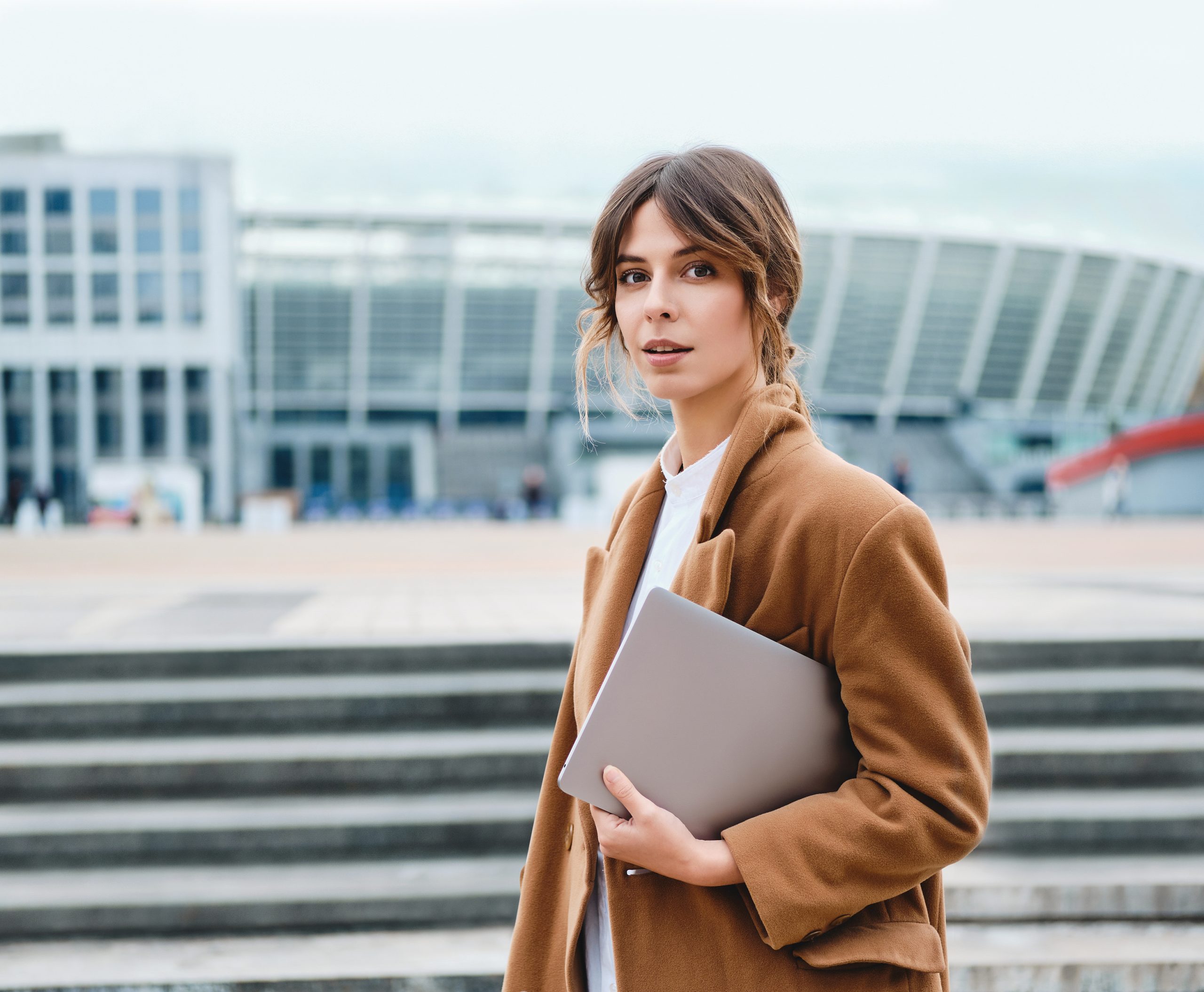 Young beautiful stylish businesswoman in coat with laptop though