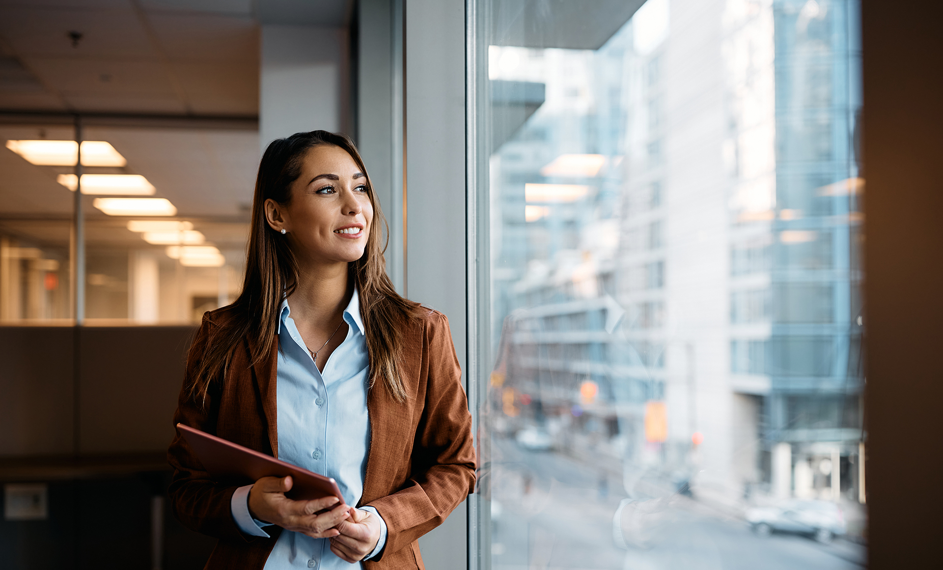 Pensive businesswoman with touchpad looking through window while working in office.